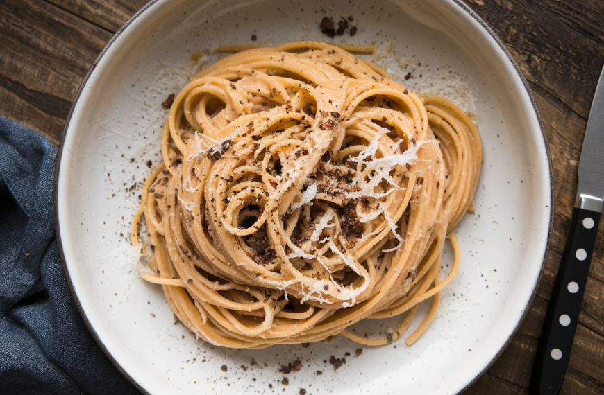 En tallerken med cacio e pepe – italiensk pasta med ost og sort pepper, servert på en mørk keramikkplate.