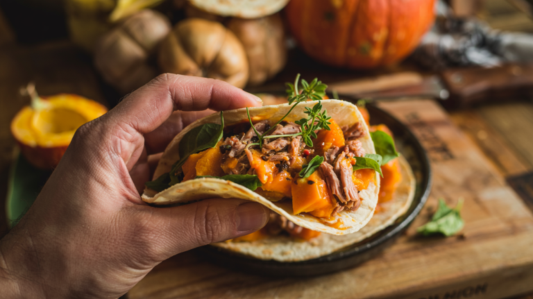 Taco fylt med pulled secreto Iberico-svinekjøtt og ovnsbakt Hokkaido-gresskar, holdt i hånd over rustikt kjøkkenbord.