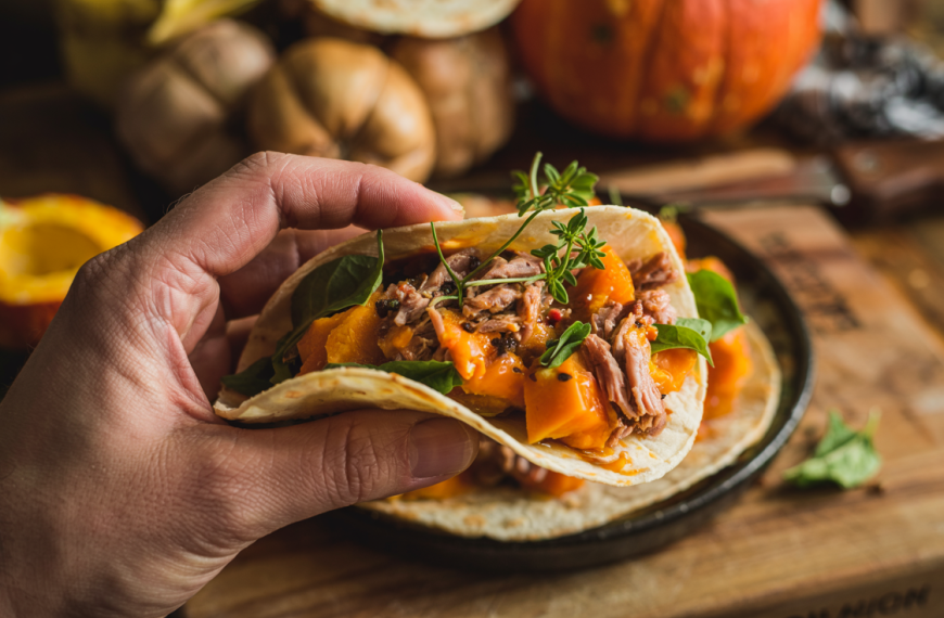 Taco fylt med pulled secreto Iberico-svinekjøtt og ovnsbakt Hokkaido-gresskar, holdt i hånd over rustikt kjøkkenbord.
