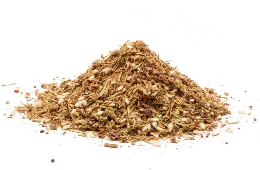 Za’atar-krydderblanding med sumak, timian, svart spisskummen, koriander, sesamfrø, Aleppo chili og gresk oregano, presentert på en hvit bakgrunn.