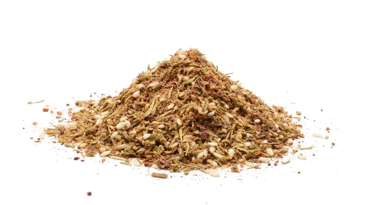 Za’atar-krydderblanding med sumak, timian, svart spisskummen, koriander, sesamfrø, Aleppo chili og gresk oregano, presentert på en hvit bakgrunn.
